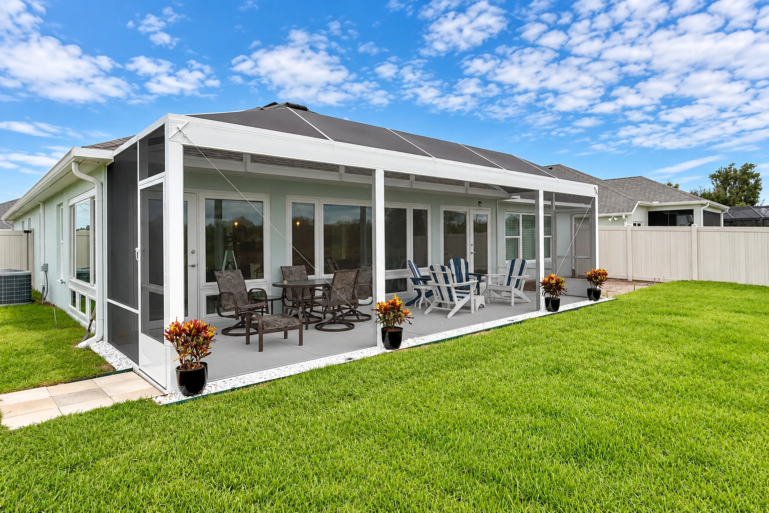 Enclosed patio room with white-framed screens, outdoor seating, and a lawn under a blue sky.